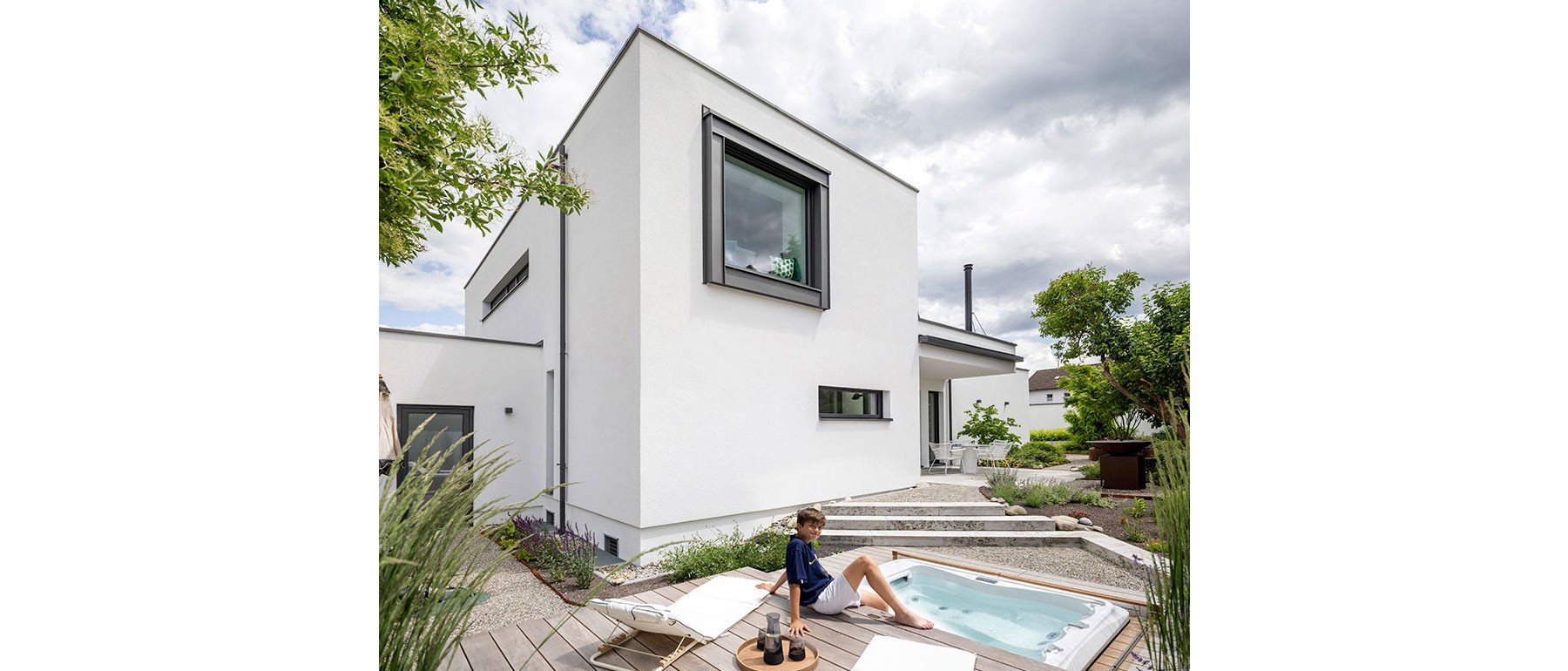 Offener Wohnbereich im modernen Holzhaus mit bodentiefen Fenstern und Blick auf den begrünten Innenhof 