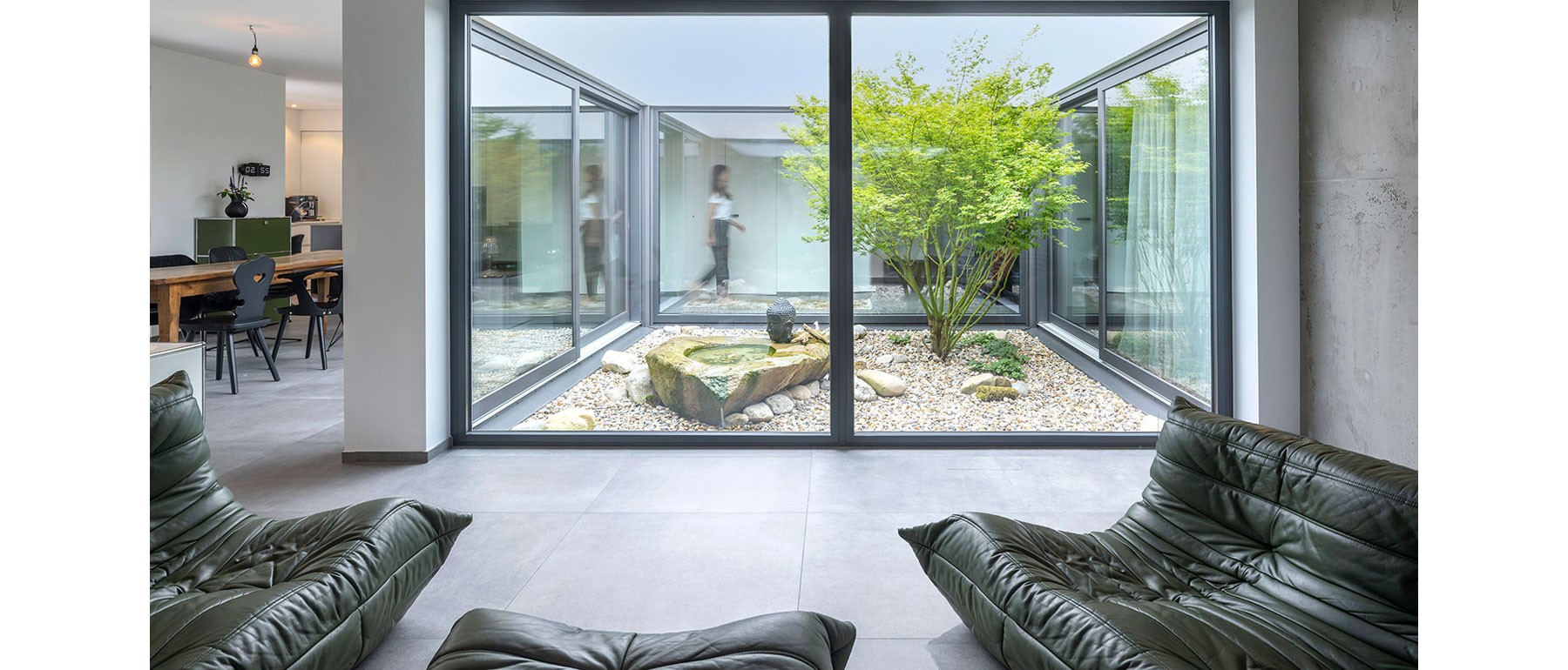 Gemütlicher Wohnbereich im nachhaltigen Atriumhaus mit modernem Kaminofen und Ausblick ins Atrium 